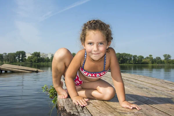 Im Sommer bei strahlendem Sonnenschein auf der Seebrücke sitzt ein kleines Mädchen — Stockfoto
