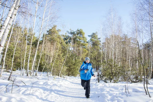 In inverno, in una luminosa giornata di sole, un ragazzo corre attraverso la foresta . — Foto Stock