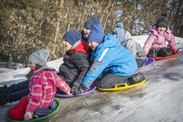 In inverno, in una luminosa giornata di sole, una folla di bambini scivola dow — Foto Stock