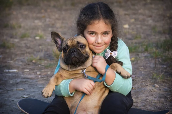 In the autumn park, a little girl holds a French bulldog in her — Stock Photo, Image
