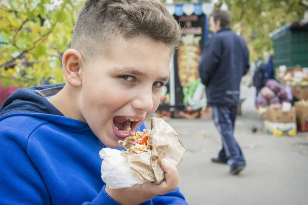 In the summer, on the street, the boy eats fast food. — Stock Photo, Image