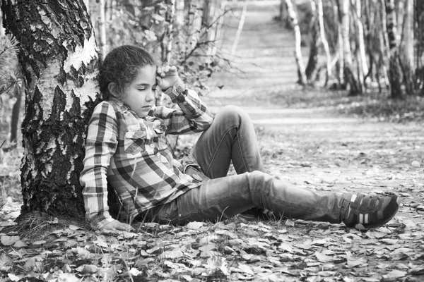 W jesiennym lesie brzozowym, mała smutna dziewczynka siedzi pod — Zdjęcie stockowe