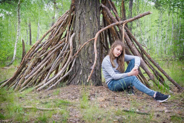 在一个阴天的夏天 一个女孩坐在一个用树枝搭成的茅屋附近的森林里 — 图库照片