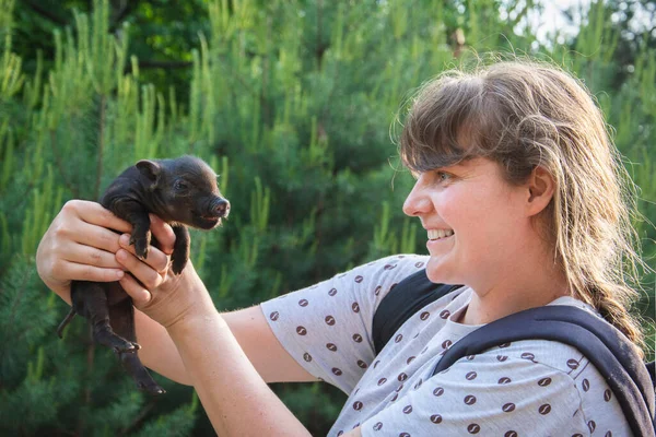 明るい晴れた日に村の夏には 女の子は彼女の手に小さな豚を保持しています — ストック写真