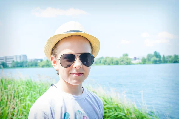 夏の晴れた日には 湖の近くに眼鏡と帽子の女の子が立っています — ストック写真