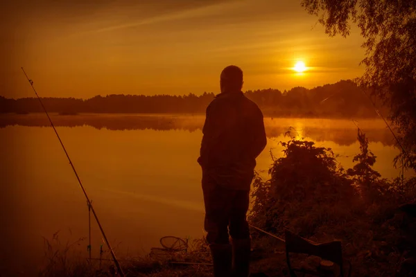 湖の夜明けに夏の朝 釣り竿の隣の岸に漁師が立っている — ストック写真