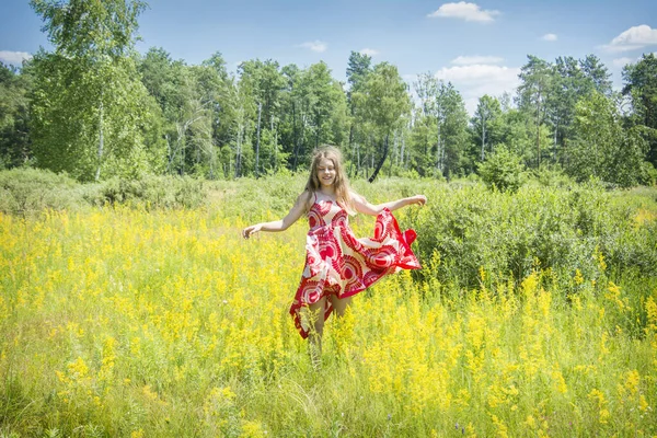 夏には 晴れた日には 開花したフィールドで 女の子は風から発生する明るい赤のドレスに立っています — ストック写真