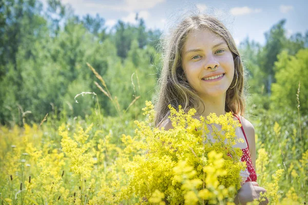 在一个阳光灿烂的日子里 在一片繁茂的田野里 一个姑娘站在从风中飘扬出来的鲜红的裙子上 手里捧着一束黄色的花 — 图库照片