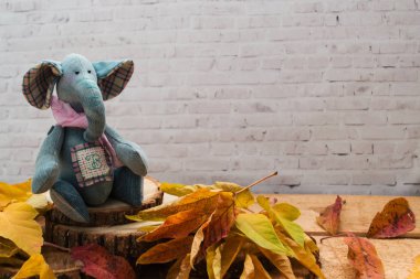 Denim Tekstil fil, oyuncak Ahşap Testereleri, sarı sonbahar yaprakları etrafında oturur.