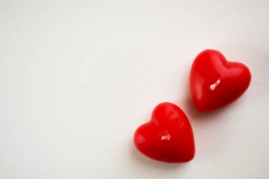 Valentine's day background with red candles in the shape of a heart, border of felt large hearts on a white table, flat lay clipart