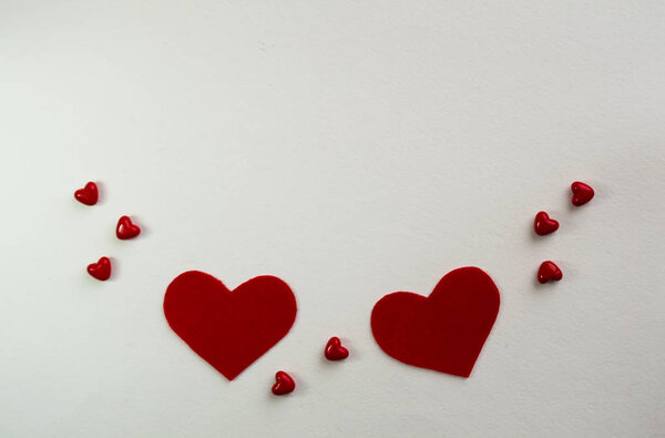 Valentine's Day background with red hearts, borders of large and small felt hearts on a white table, flat lay