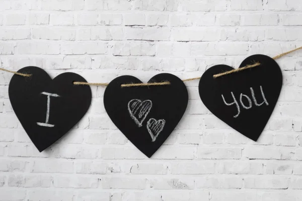 Greeting card Valentine. Three hearts hang on a rope, on a brick light wall. The composition of the inscription for Valentine\'s Day or for the wedding - I love you.