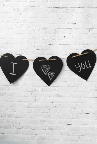 Greeting card Valentine. Three hearts hang on a rope, on a brick light wall. The composition of the inscription for Valentine\'s Day or for the wedding - I love you.
