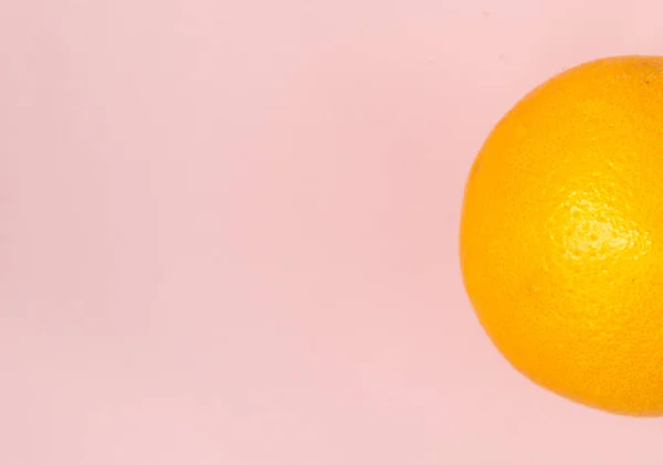 Una naranja sobre un fondo rosa. Hay un lugar para el texto . — Foto de Stock