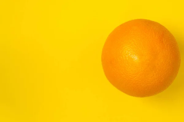 Una naranja sobre un fondo amarillo. Hay un lugar para el texto . — Foto de Stock