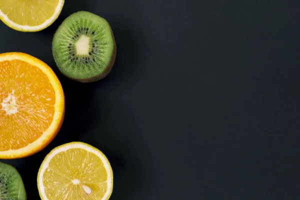 Trozos de kiwi, limón y naranja sobre un fondo negro, sobre una pizarra de tiza. Hay un lugar para el texto . — Foto de Stock