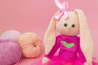 Örme pembe tavşan el yapımı. Paskalya tavşanı, pembe örme bir kazak ve pembe bir etek. İplik ve pembe çiçekler topları arasında oturur,