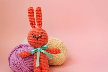 Turuncu örme tavşan pembe bir arka planda iplik çok renkli topları arka planda duruyor. Metin için bir yer var.