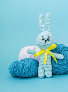 Örme mavi tavşan el yapımı, mavi ve beyaz iplik bir arka planda duruyor, ve mavi bir arka plan üzerinde. Metin için bir yer var.