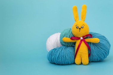Turuncu örme tavşan mavi bir arka plan üzerinde iplik çok renkli topları arka planda duruyor. Metin için bir yer var.