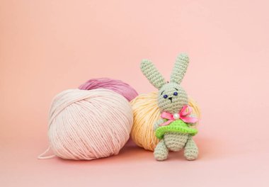 Gri örme tavşan pembe bir arka plan üzerinde iplik çok renkli topları arka planda duruyor. Metin için bir yer var.