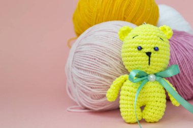 Renkli bir örme ayı monokromatik renkli bir arka plan üzerinde oturuyor, arkasında farklı iplik bir skein, metin için bir yer var.