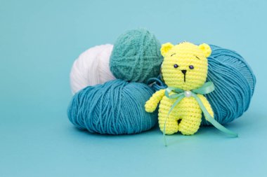 Renkli bir örme ayı monokromatik renkli bir arka plan üzerinde oturuyor, arkasında farklı iplik bir skein, metin için bir yer var.