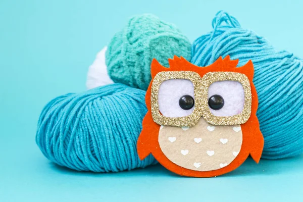 Kendinden yapılmış yumuşak oyuncak baykuş keçe yapılmış, bir renk monofonik arka plan üzerinde. Baykuş iplik topları yanında duruyor. Metin için bir yer var.