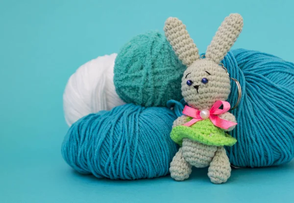 Gri örme tavşan mavi bir arka plan üzerinde iplik çok renkli topları arka planda duruyor. Metin için bir yer var.