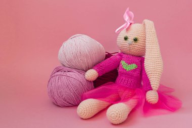 Örme pembe tavşan el yapımı. Paskalya tavşanı, pembe örme bir kazak ve pembe bir etek. İplik ve pembe çiçekler topları arasında oturur,