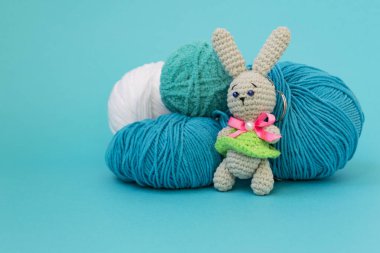 Gri örme tavşan mavi bir arka plan üzerinde iplik çok renkli topları arka planda duruyor. Metin için bir yer var.