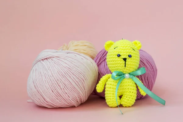 A colored knitted bear is sitting on a monochromatic colored background, behind it is a skein of different yarn, There is a place for text.