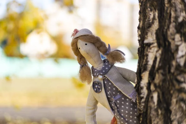 Une poupée Tilda femelle dans une robe colorée regarde derrière un arbre. Enregistrement des vacances. Intérieur poupée de fée fait main. Art et créativité. Fond flou — Photo