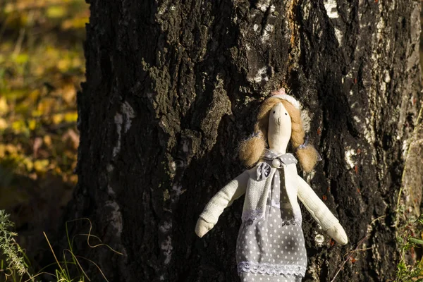 Une poupée Tilda femelle en vêtements colorés se tient près d'un tronc de bouleau. Enregistrement des vacances. Intérieur poupée de fée fait main. Art et créativité. Fond flou . — Photo