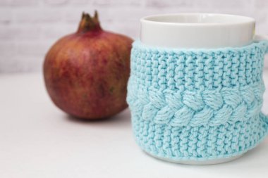 Kırmızı bir garnat ile örme mavi durumda bir fincan, hafif bir arka plan üzerinde meyve. Konfor, rahatlama, sağlıklı gıda kavramı. İskandinav tarzı. Test için bir yer var..