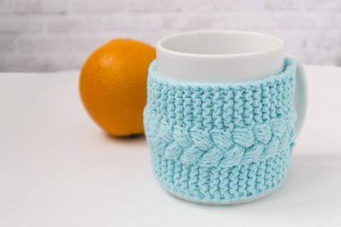 Açık bir arka plan üzerinde turuncu bir mandalina ile örme mavi durumda bir fincan. Konfor, rahatlama, sağlıklı gıda kavramı. İskandinav tarzı. Test için bir yer var..