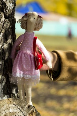 Renkli giysiler içinde bir kadın Tilda bebek bir huş ağacı gövde yakınında duruyor. Tatil kaydı. İç peri bebek el yapımı. Sanat ve yaratıcılık. Bulanık arka plan.