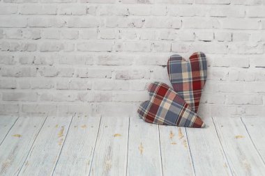 Damalı kumaştan iki el yapımı kalpler hafif tuğla arka plan üzerinde durmak ve ahşap bir masanın hafif bir arka plan üzerinde. Aşk kavramı, tebrikler, el emeği needlewoman.