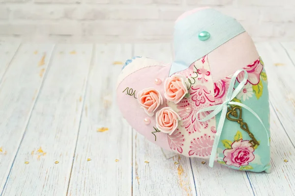 Ein textiles Herz mit romantischer Blütenfarbe auf schlichtem hellen Holzgrund. Selektiver Fokus. Shabby Chic Stil. — Stockfoto
