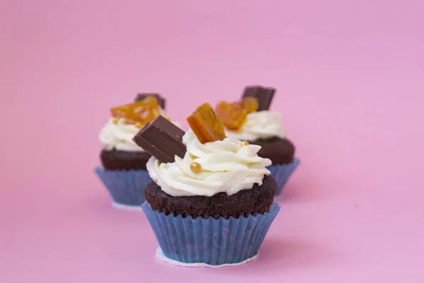 Drie heerlijke cupcakes op een roze achtergrond. Witte lucht crème taart versierd met chocolade en gecandied fruit. Cupcakes in blauwe papieren cups. Er is een plaats voor tekst. Stockfoto