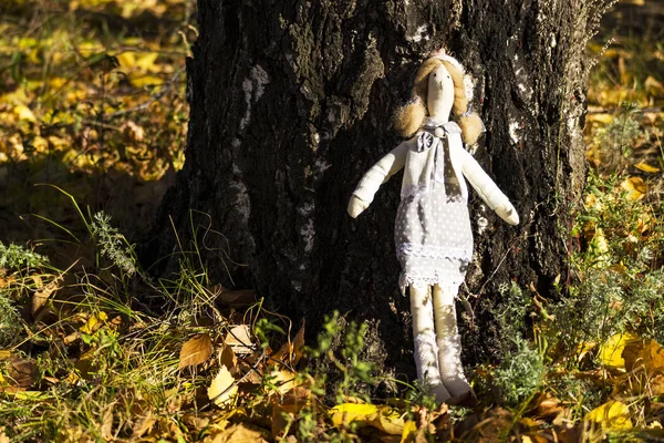 A female Tilda doll in colorful clothes is standing near a birch tree trunk. Registration of holidays. Interior fairy doll handmade. Art and creativity. Blurred background. Royalty Free Stock Photos