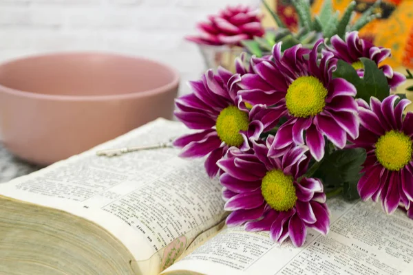 Pink chrysanthemum flowers lie on the table on an open book. Nearby is a silver key.