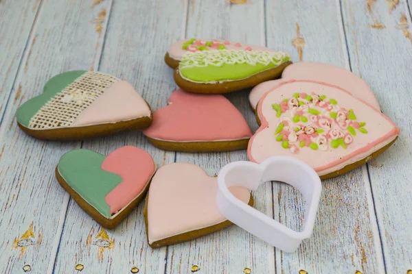 Pink and colored gingerbread and honey cakes and heart-shaped cookies lie in a messy pile on a light wooden background. Nearby are white molds for baking. Place for text. The concept of love, mother\'s