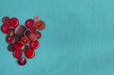 Dikiş düğmeleri turkuaz monofonik arka plan üzerinde bir kalp şeklinde yatıyor. Aşk kavramı, iğne işi, duygular.