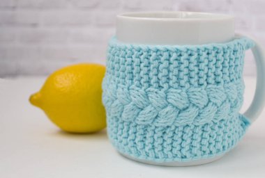 Hafif bir arka planda sarı limon ile örme mavi bir durumda bir fincan. Konfor, rahatlama, sağlıklı gıda kavramı. İskandinav tarzı. Test için bir yer var.