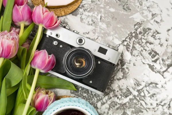 Eski kamera beton bir masaüzerinde yatıyor, sıcak çay ile bir fincan yanında, yanında lale çiçekleri pembe bir buket vardır. Konsept kahvaltı, instagram, seyahat.