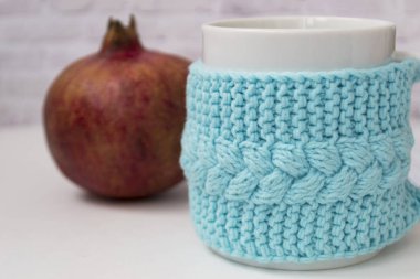 Kırmızı bir garnat ile örme mavi durumda bir fincan, hafif bir arka plan üzerinde meyve. Konfor, rahatlama, sağlıklı gıda kavramı. İskandinav tarzı. Test için bir yer var..