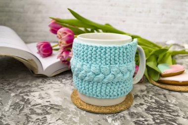 Açık bir kitap ile bir örme mavi durumda çay beyaz fincan ve pembe çiçekler ile lale ve tatlılar, bir dokusal masada Gingerbread ile.