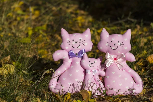 Drei Textilspielzeuge einer Katze, die zusammen auf einem gelben Laub auf einer Wiese sitzen. Familienkonzept, Kinderschutz. Rommé Hintergrund. — Stockfoto