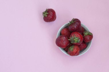 Bir tabak içinde Olgun kırmızı çilek. Pembe arka plan. Vitaminler ile gıdalar.